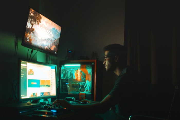 Streamer at computer with multiple monitors and colorful lighting