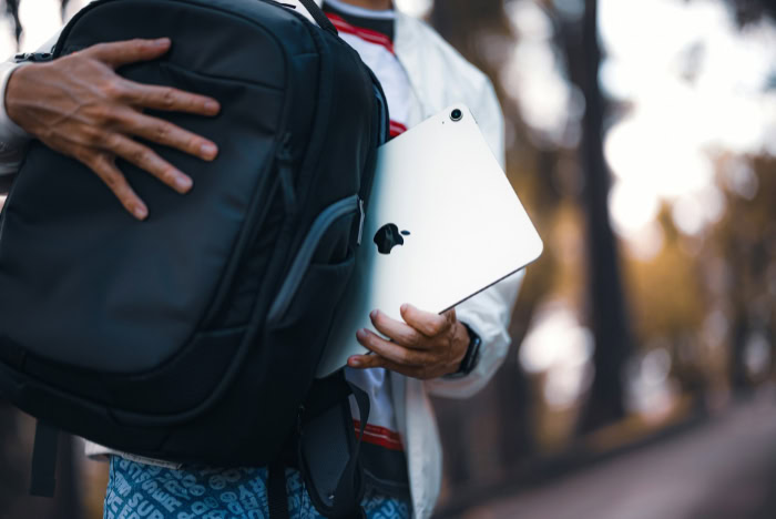 Student with backpack holding white iPad outdoors