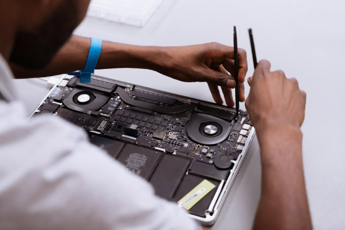Technician repairing a laptop motherboard with tools resized