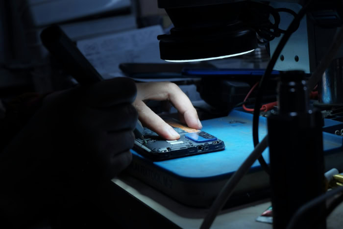 Technician repairing smartphone internals under desk lamp light