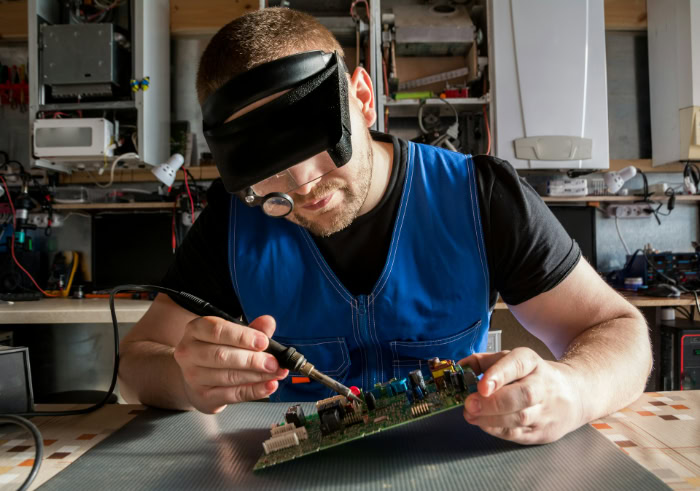 Technician soldering electronic circuit board wearing magnifier resized