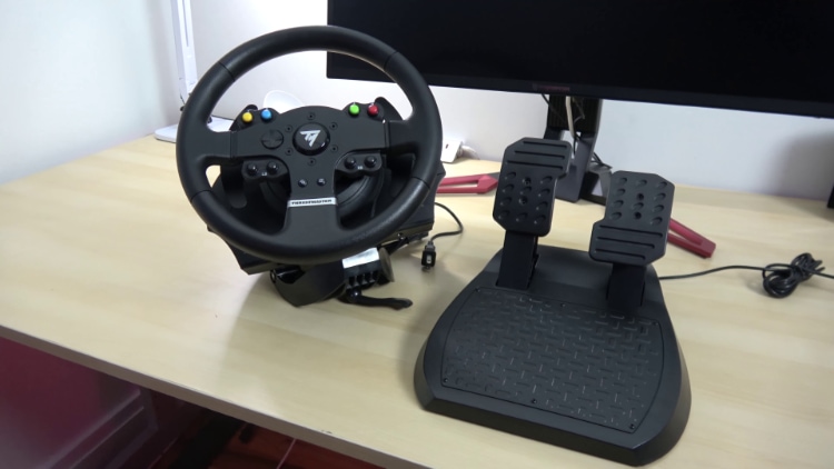Black Thrustmaster TMX near black pedals on wooden table