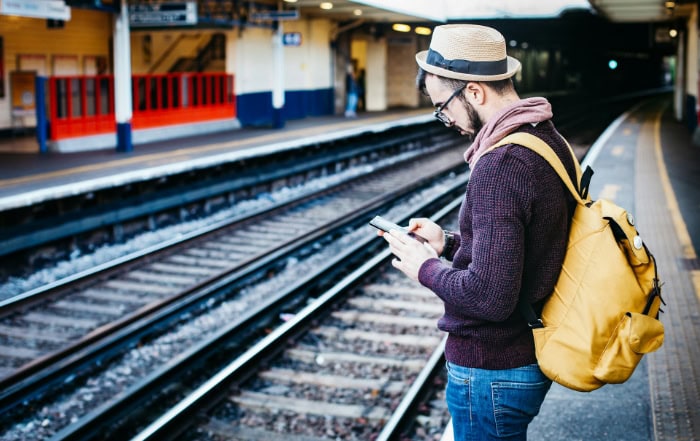 Traveler using smartphone on train platform with yellow backpack