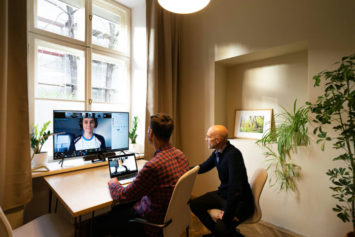 Two colleagues attending online video call on large monitor