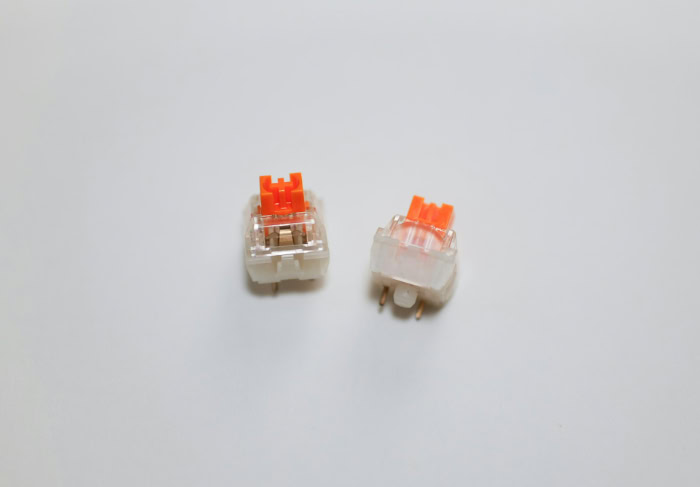 Two orange stem mechanical keyboard switches on white surface