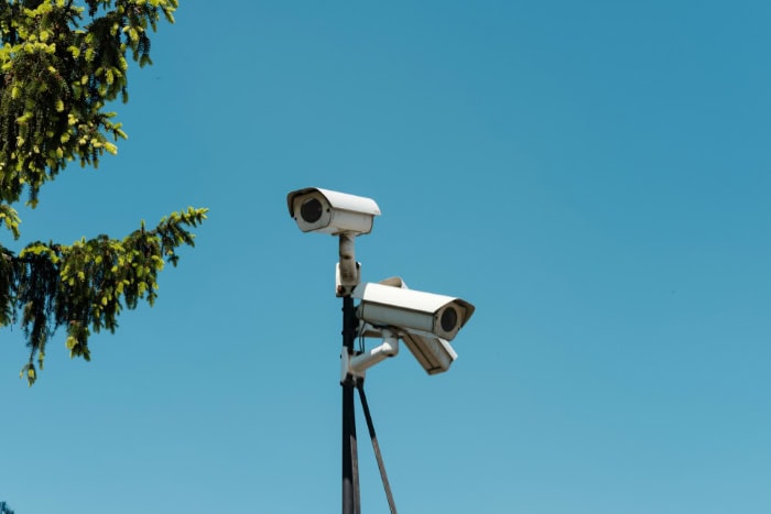 Two white security cameras mounted on pole against blue sky