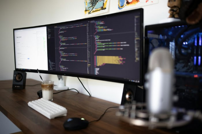 Ultrawide monitor displaying code with white keyboard and coffee