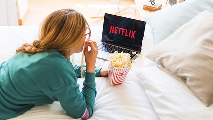 Person eating popcorn while watching netflix in bed