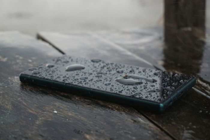 Wet smartphone with water droplets on wooden surface