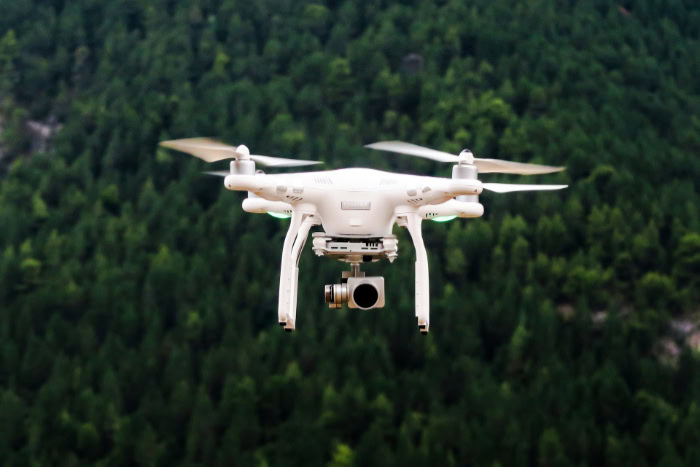White DJI Phantom drone flying over forest