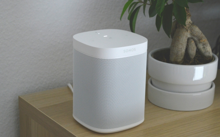 White Sonos speaker on a wooden shelf beside a potted plant