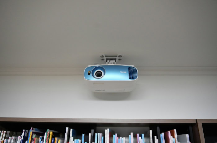 White and blue projector mounted above library bookshelf