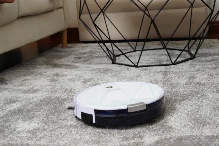 White robot vacuum cleaner cleaning a grey plush rug