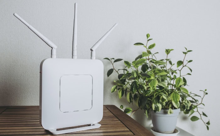 White router with antennas beside potted plant on wooden table