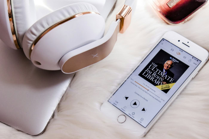 White smartphone showing Audible audiobook near gold headphones