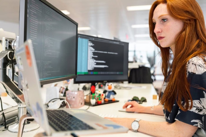 Woman coding on multiple computer screens in an office