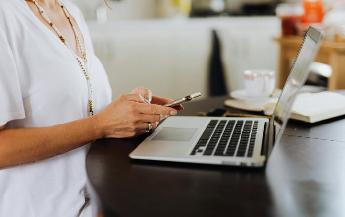 Woman in white shirt using smartphone and laptop at desk