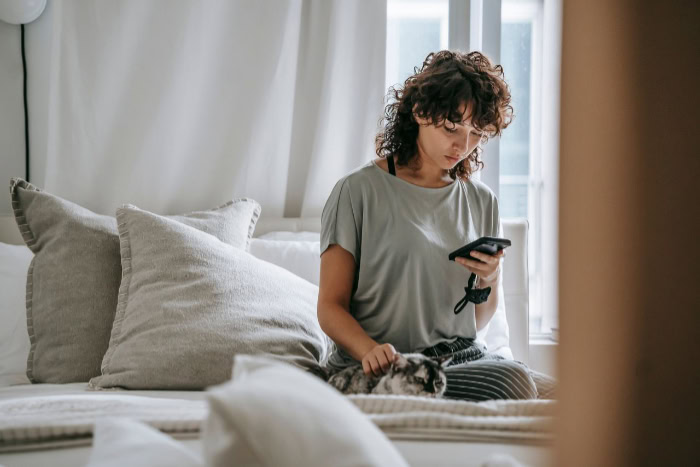 Woman on bed using smartphone and petting cat