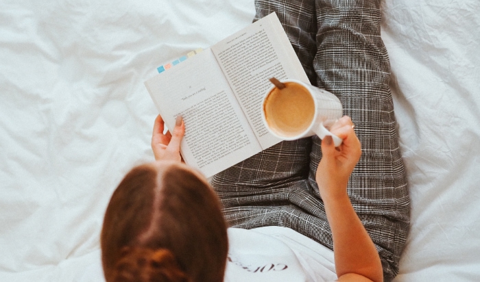 Woman reading book while holding a mug