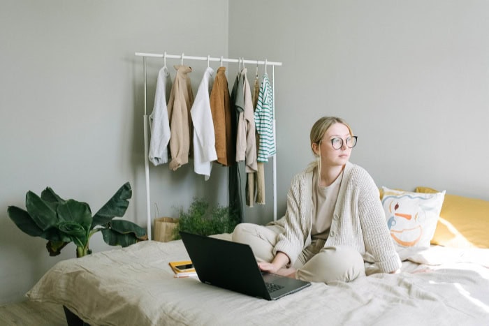 Woman sitting on bed with laptop looking away