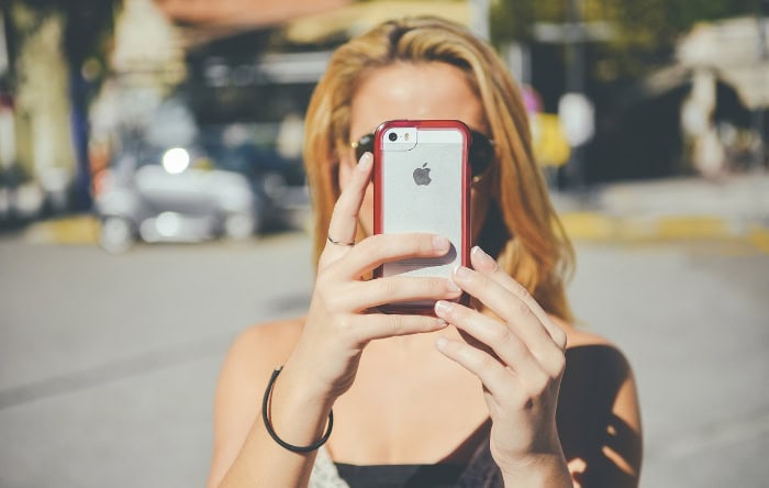 Woman taking selfie with iPhone in red protective case outdoors