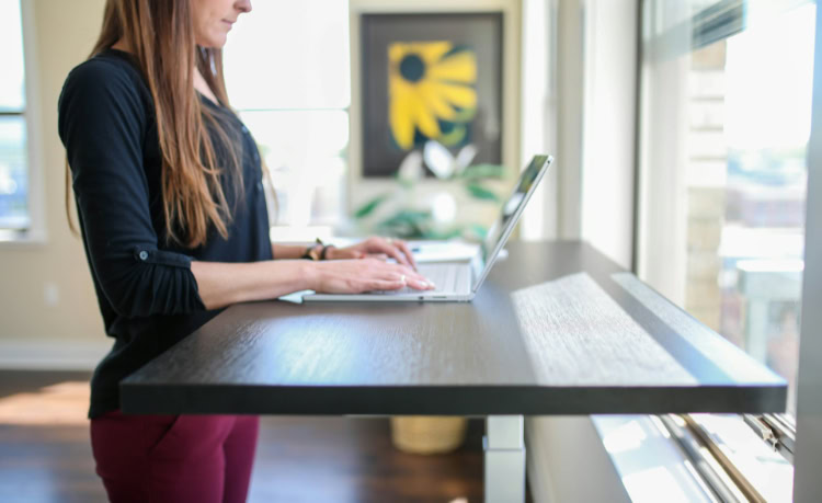 Woman typing at dark wood adjustable standing desk