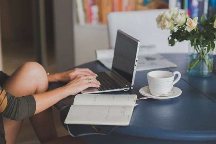 Woman typing on laptop with coffee and flowers nearby