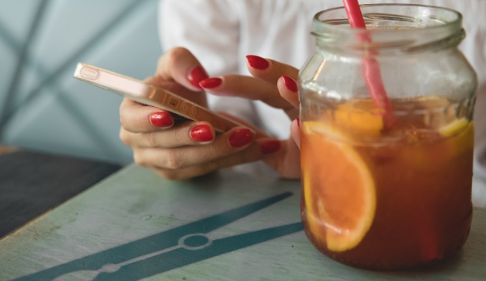 Woman using an iPhone with iced tea on the table