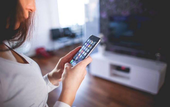 Woman using iPhone with app icons visible in living room