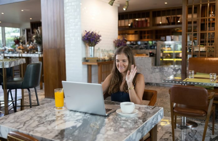 Woman using laptop in cafe smiling and waving