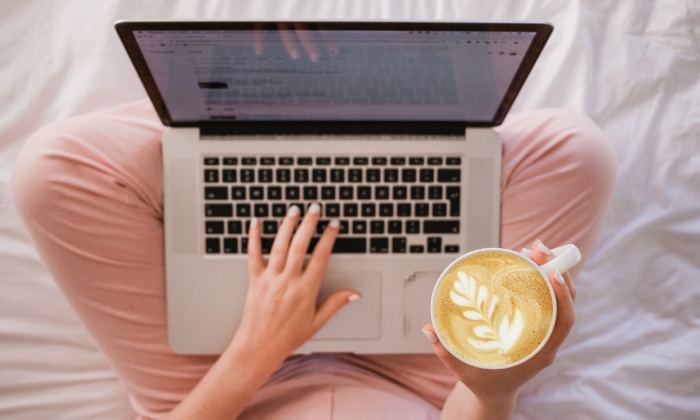 Woman using macbook while holding coffee