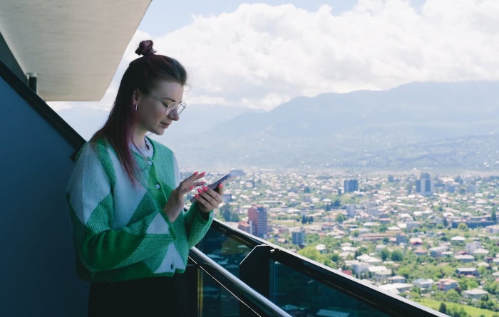 Woman using smartphone on balcony overlooking cityscape