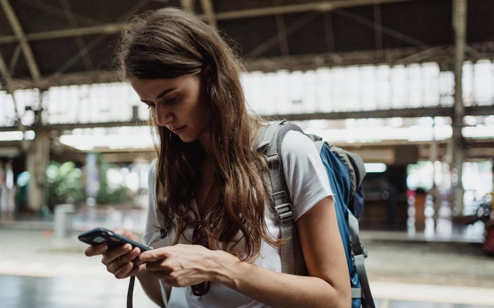 Woman using smartphone while carrying backpack in train station