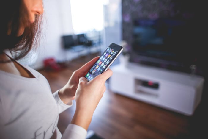 Woman using smartphone with app icons visible on screen