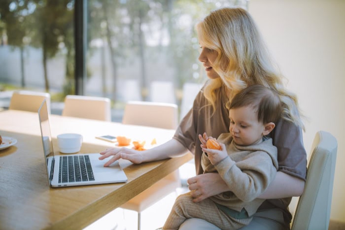 Woman working on a laptop while holding her baby