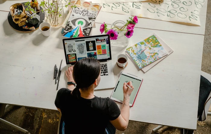 Woman working on laptop and tablet with creative materials