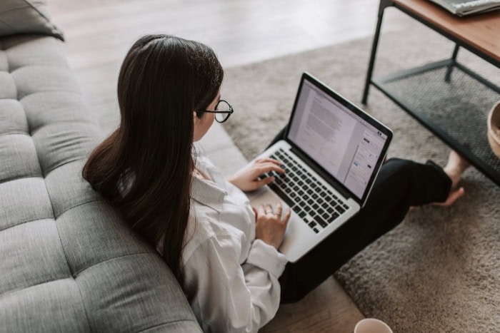 Woman working on laptop while sitting on grey couch