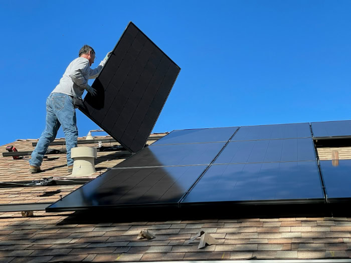 Worker lifting solar panel onto residential roof installation