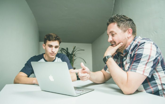 Young man teaching older man to use MacBook laptop