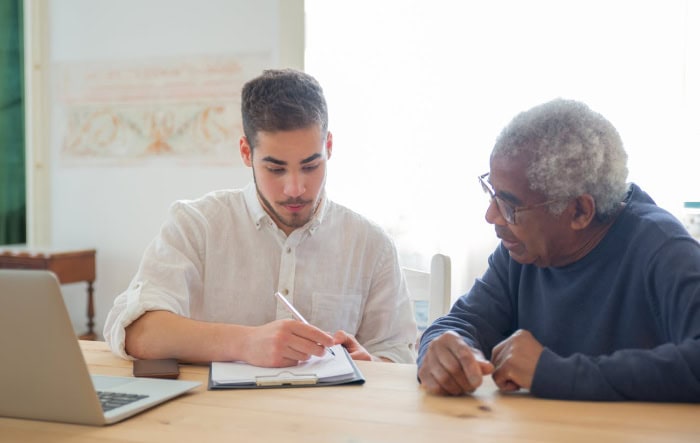 Young man teaching older man to use laptop