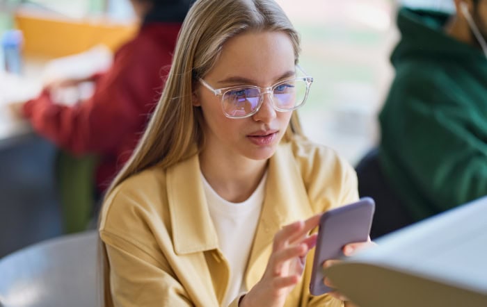 Young woman in yellow jacket using smartphone in classroom