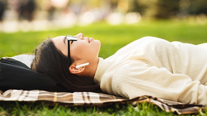 Young woman relaxing on a picnic blanket in the park wearing AirPods