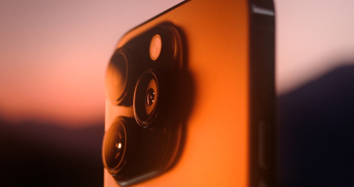 iPhone camera module silhouetted against orange sunset sky