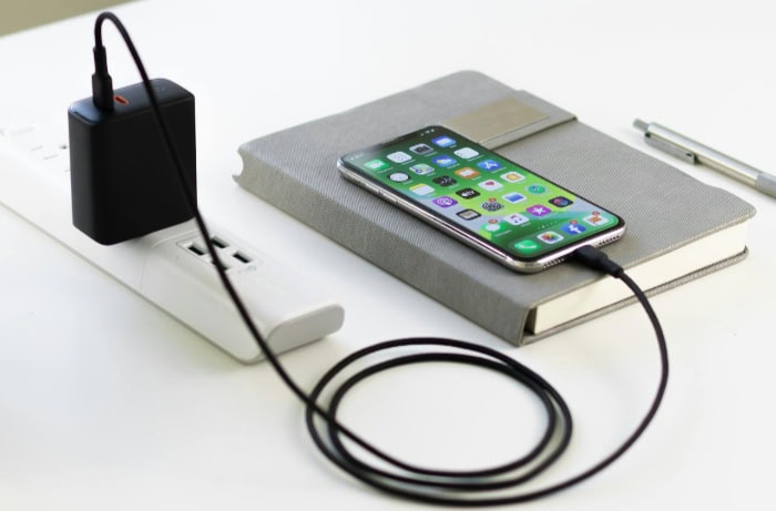 iPhone connected to black power adapter on gray notebook